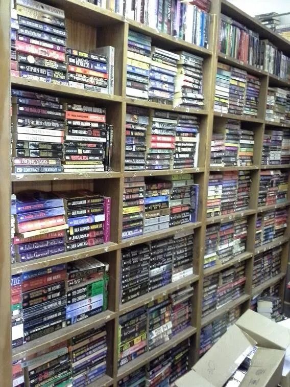 Bookshelves filled with stacked books, likely in a bookstore or library.