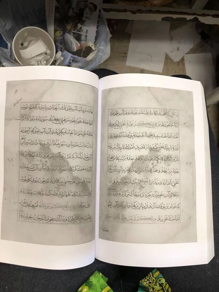 Open book with handwritten text, likely Arabic or a similar script. Gray pages, white borders.