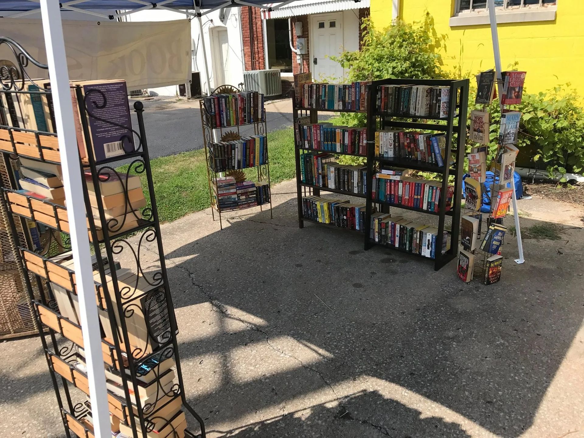 Outdoor book sale: Bookshelves display various titles. Sunlight shines on a concrete surface.
