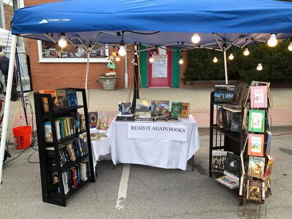 Outdoor book sale booth with blue canopy, bookshelves, and a table labeled “READING ENGINE 2020”
