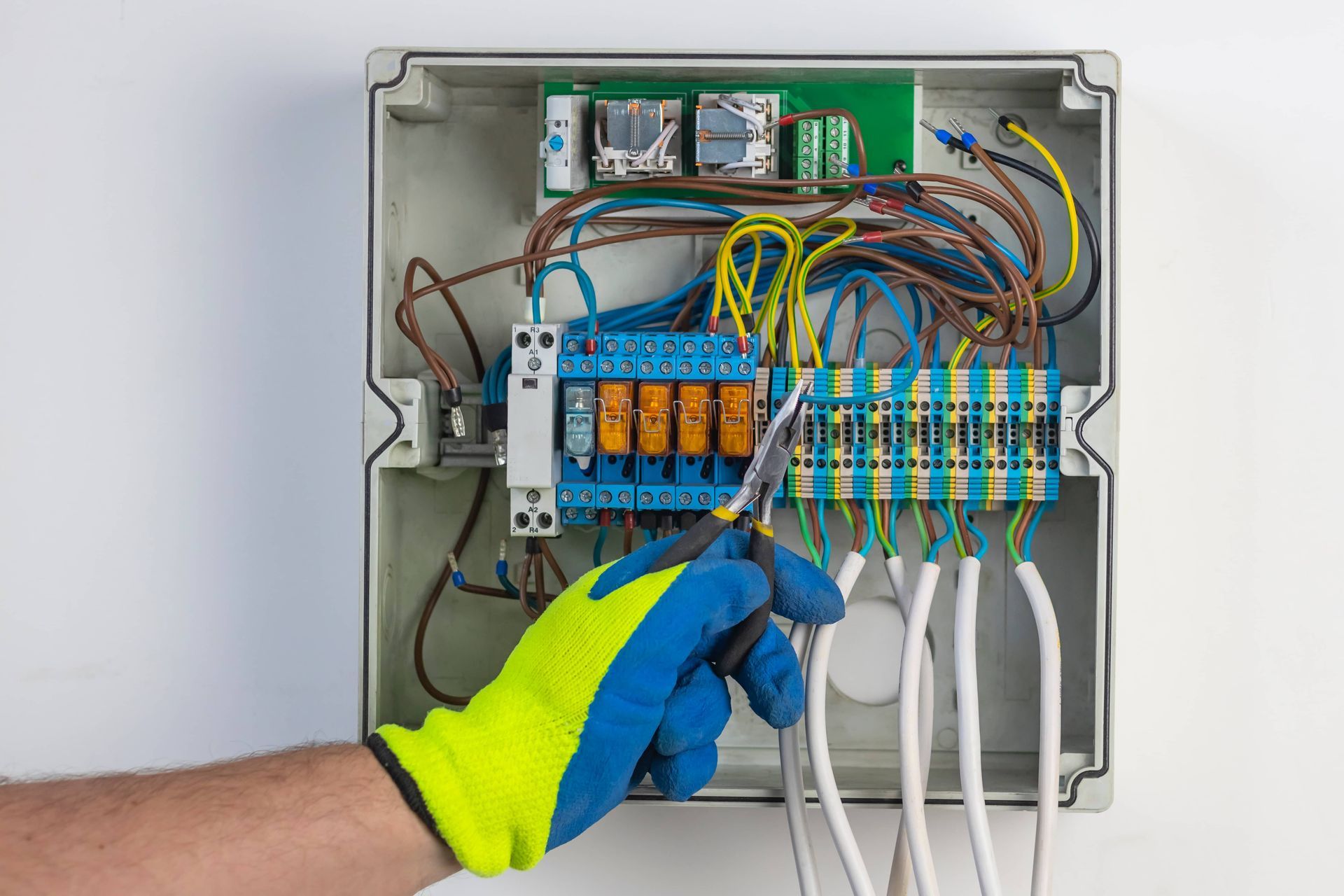 Hand wearing a glove wiring an electrical panel with colorful wires.