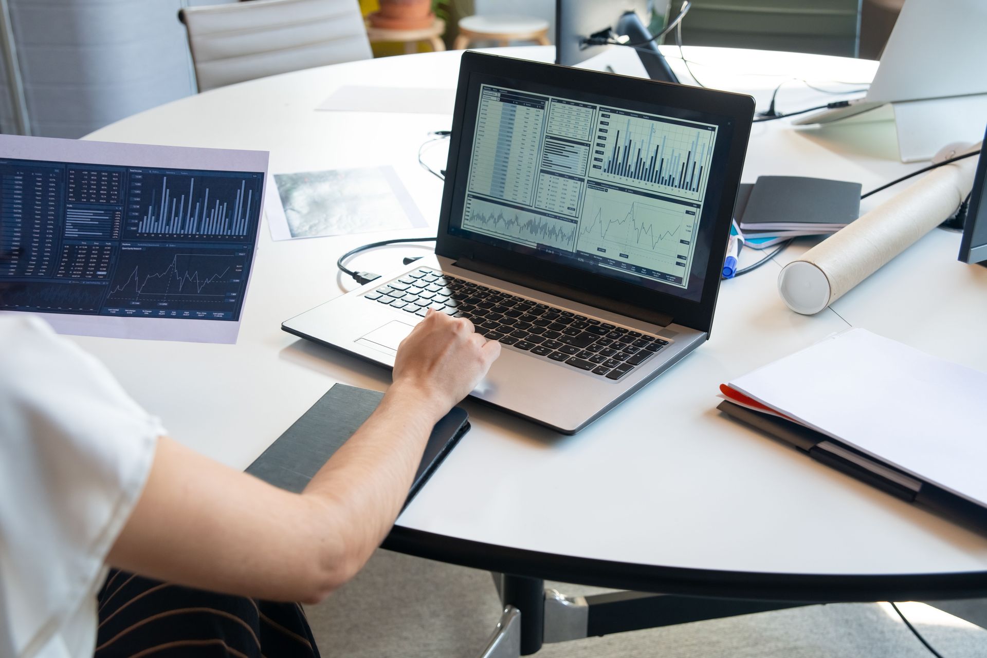 Person reviewing charts on laptop and tablet at a conference table in a bright office