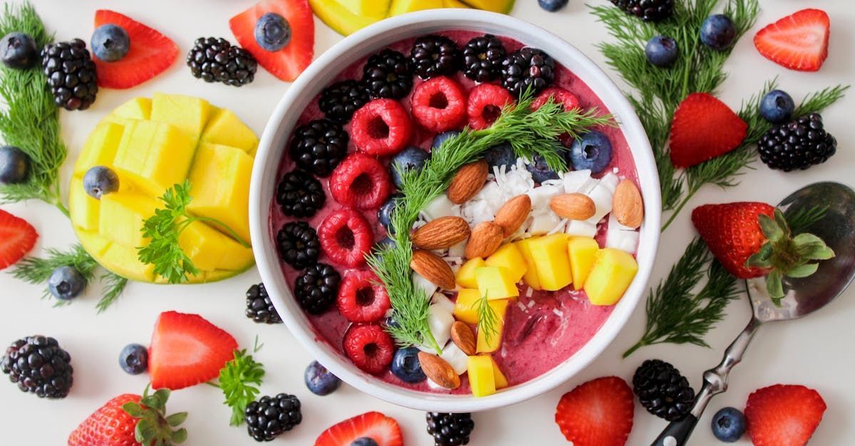 A bowl of fruit and nuts on a table surrounded by fruit.