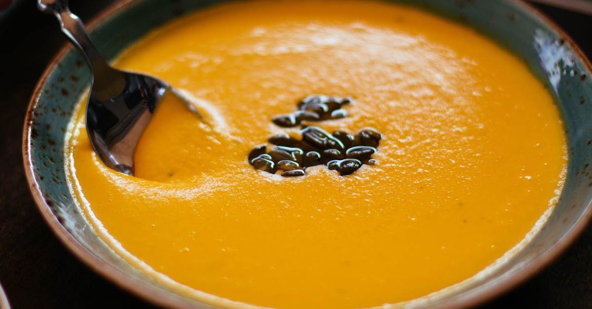 A bowl of soup with a spoon in it and pumpkin seeds on top.