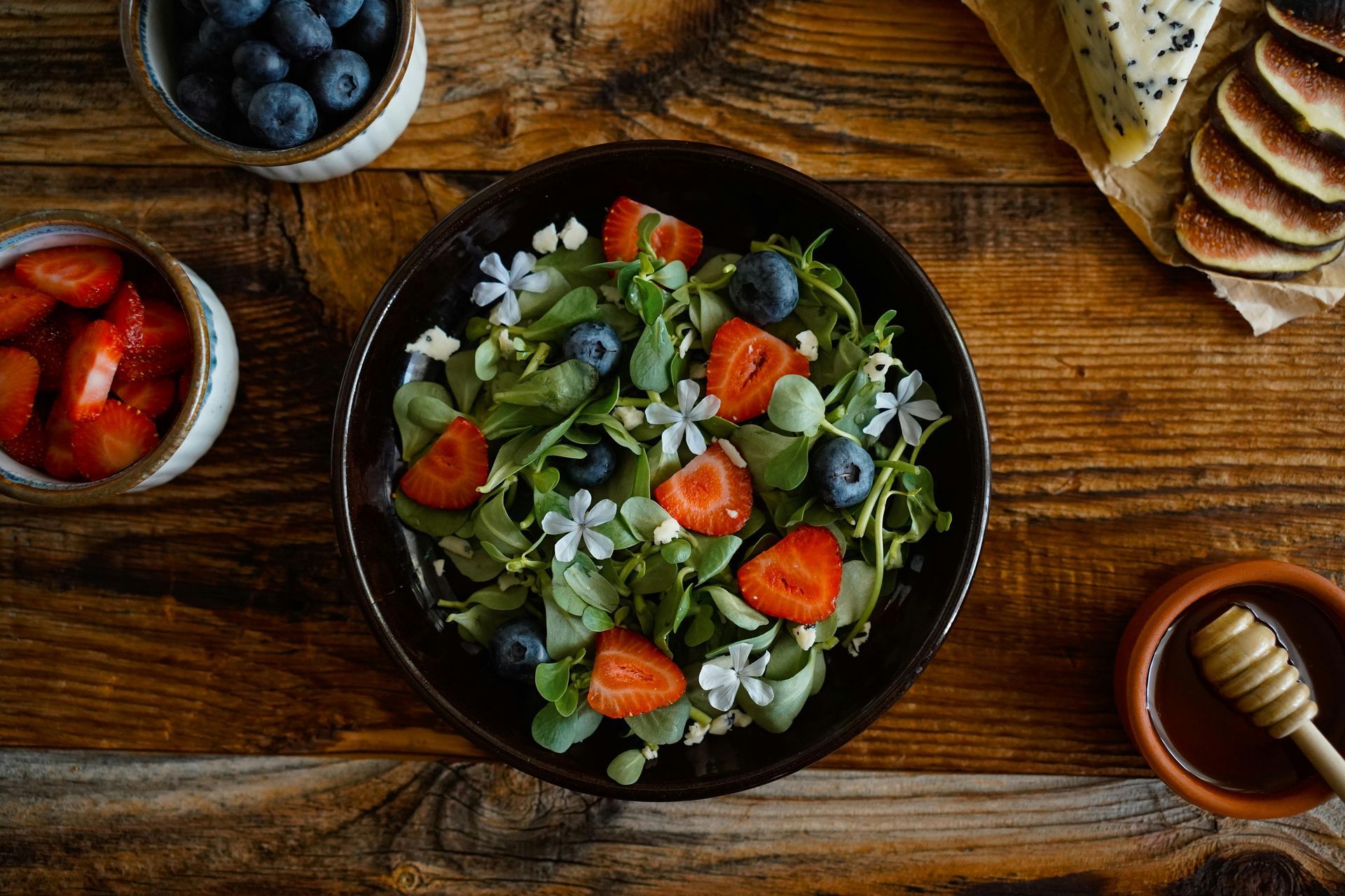 A salad with strawberries and blueberries in a bowl on a wooden table.