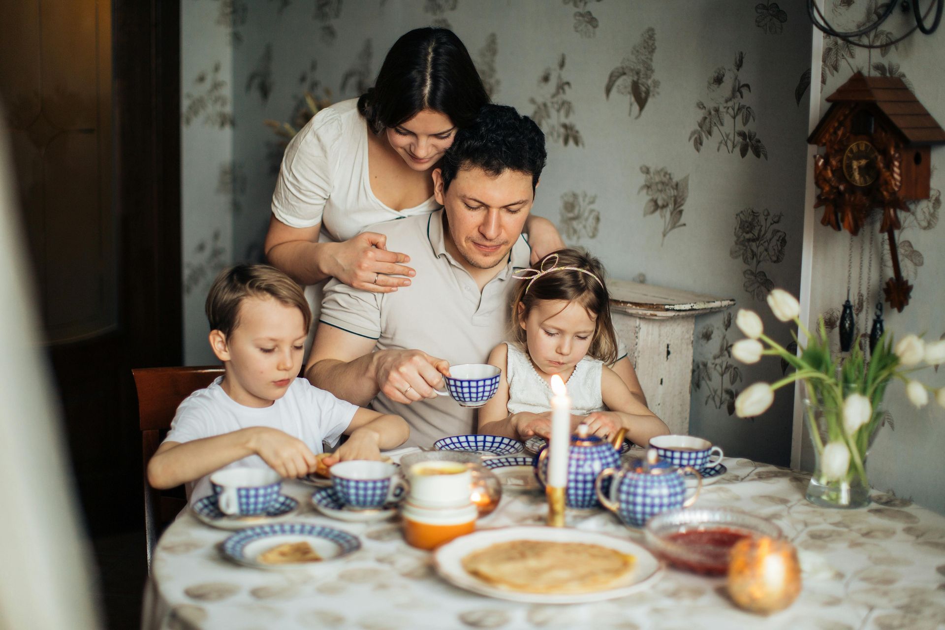 A family is sitting at a table eating pancakes and drinking tea.
