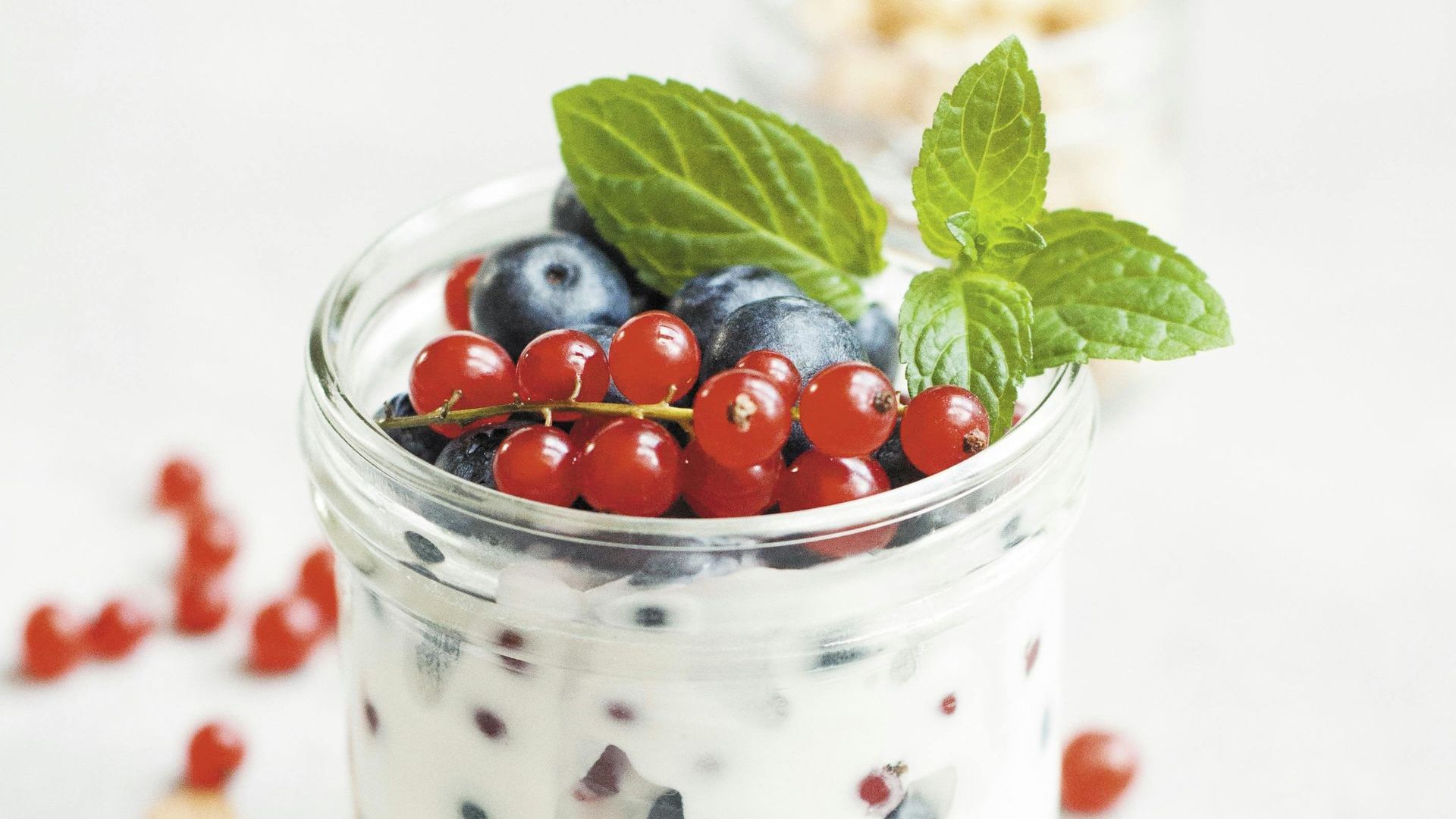 A jar of yogurt with blueberries and red currants on top.