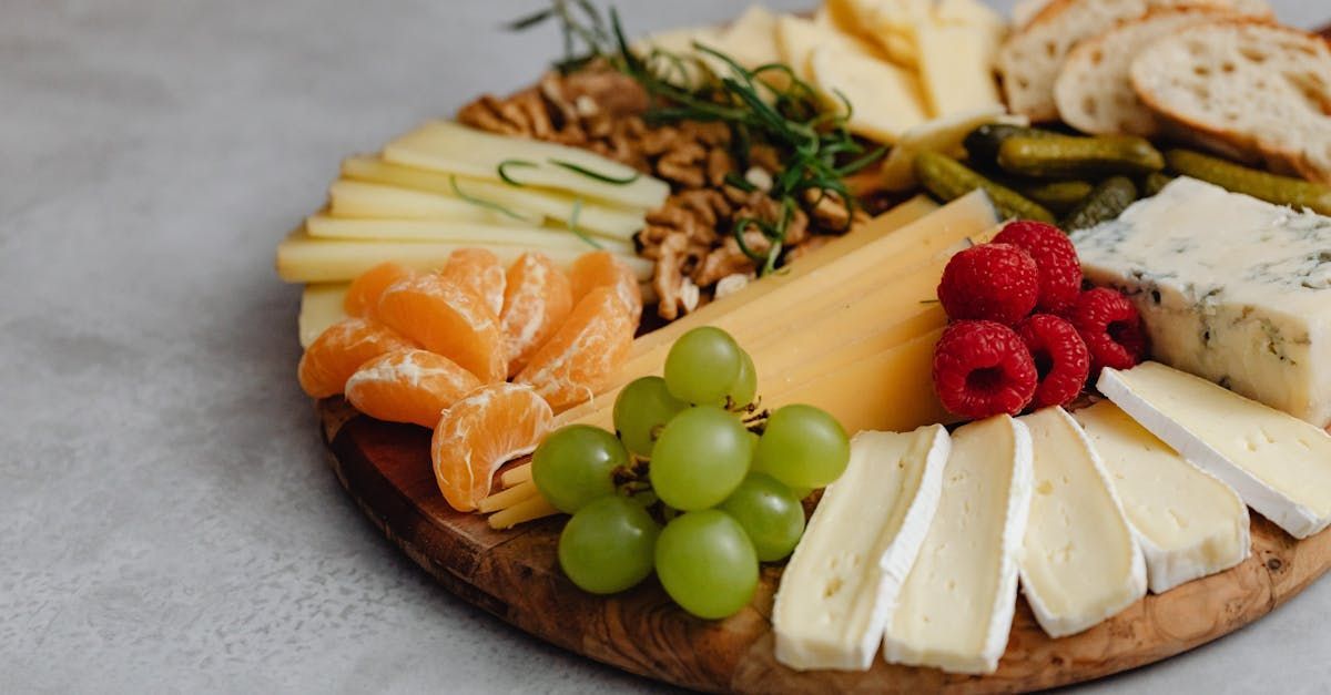 A wooden cutting board topped with cheese , grapes , raspberries , oranges and nuts.