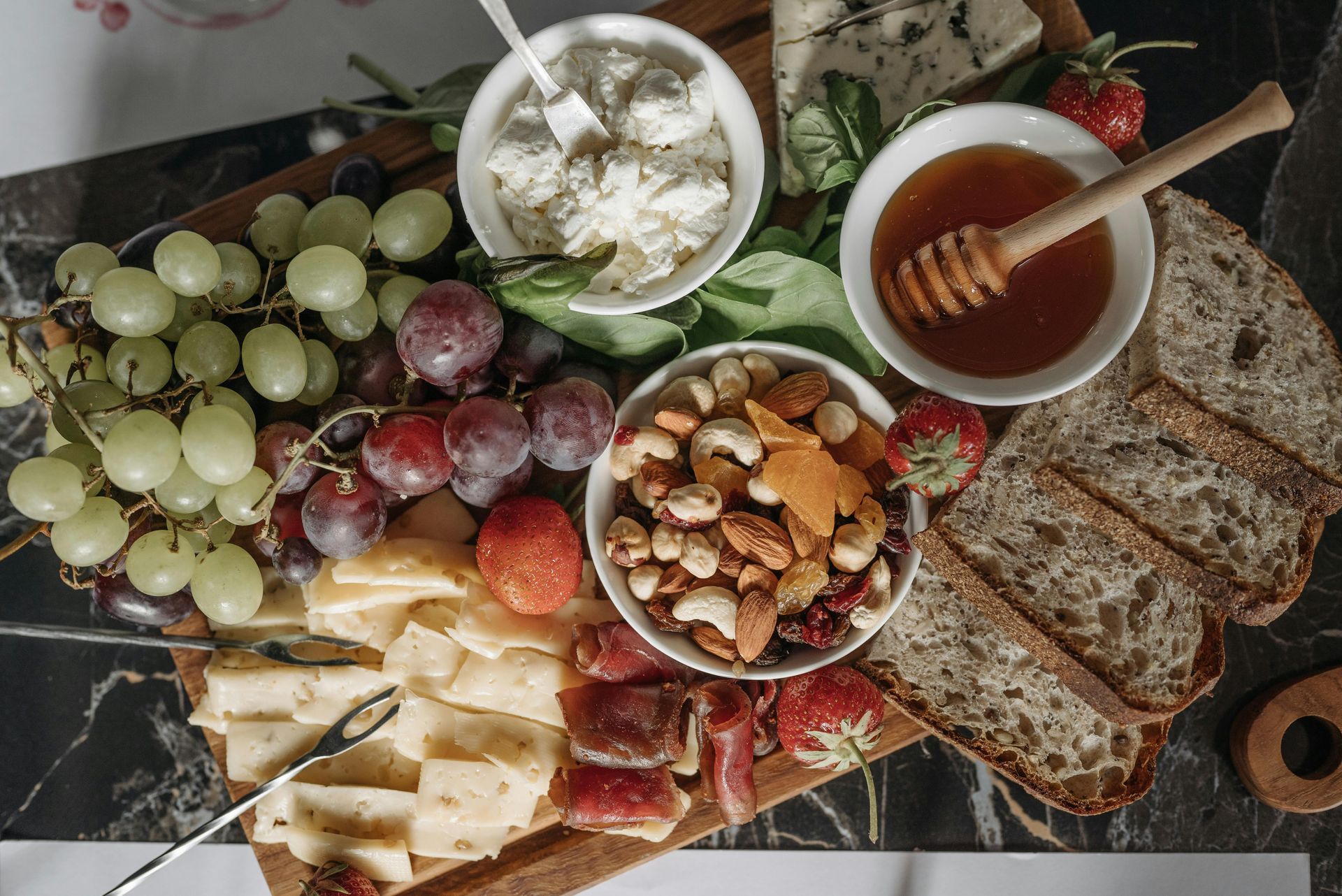 A wooden cutting board topped with cheese , grapes , nuts and honey.