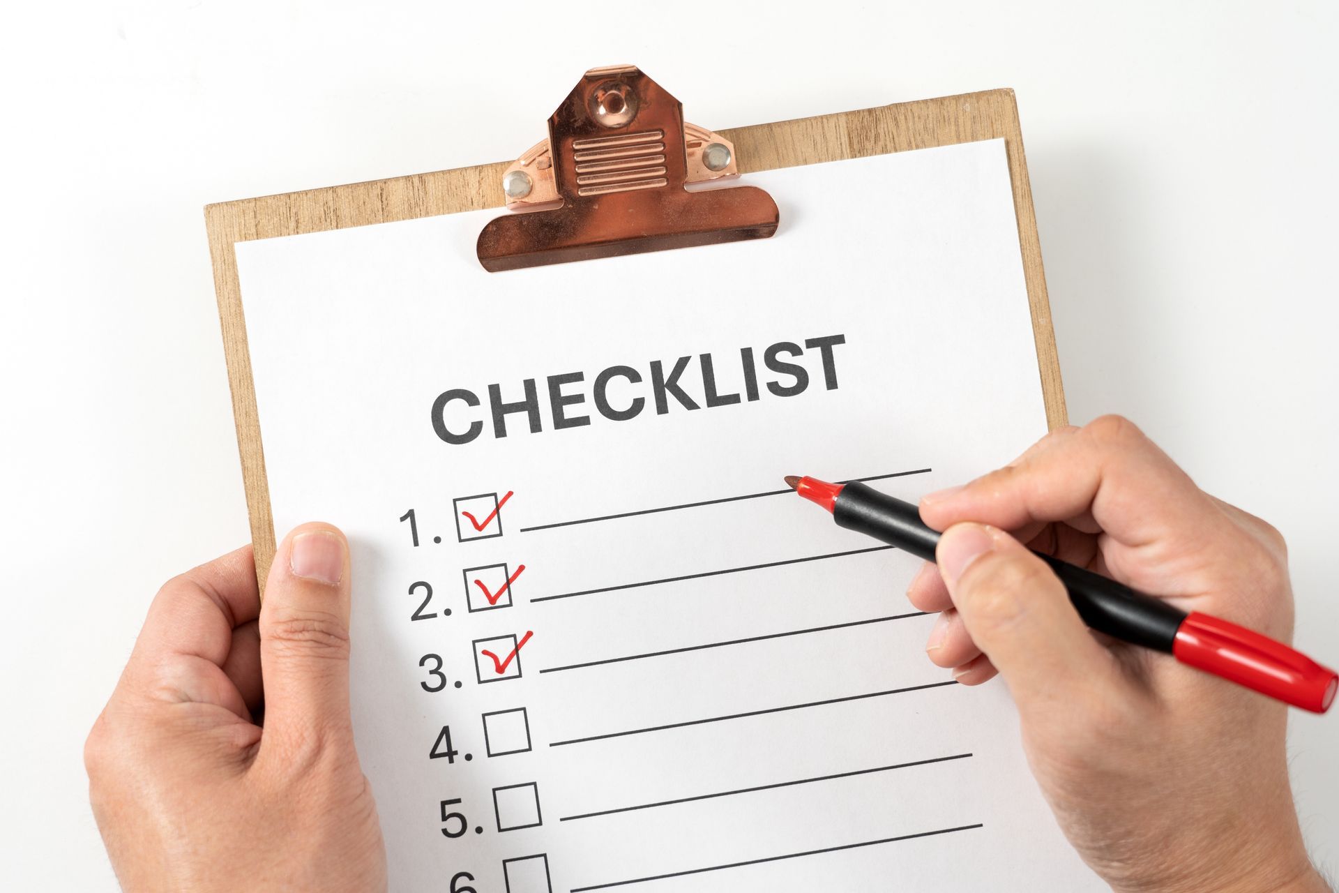 Hands checking items on a clipboard checklist with a red pen