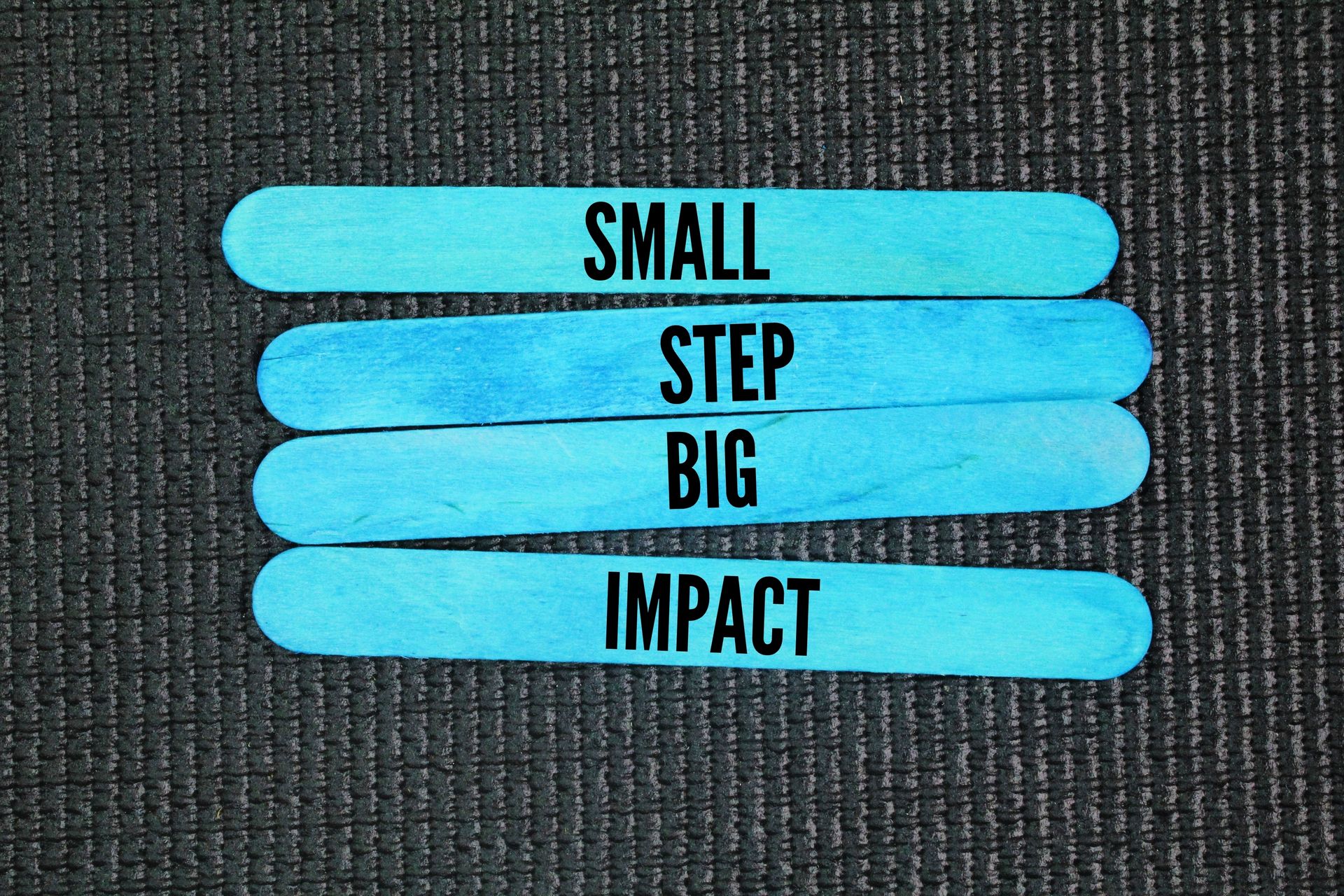 Four blue strips on dark fabric read: SMALL STEP BIG IMPACT.