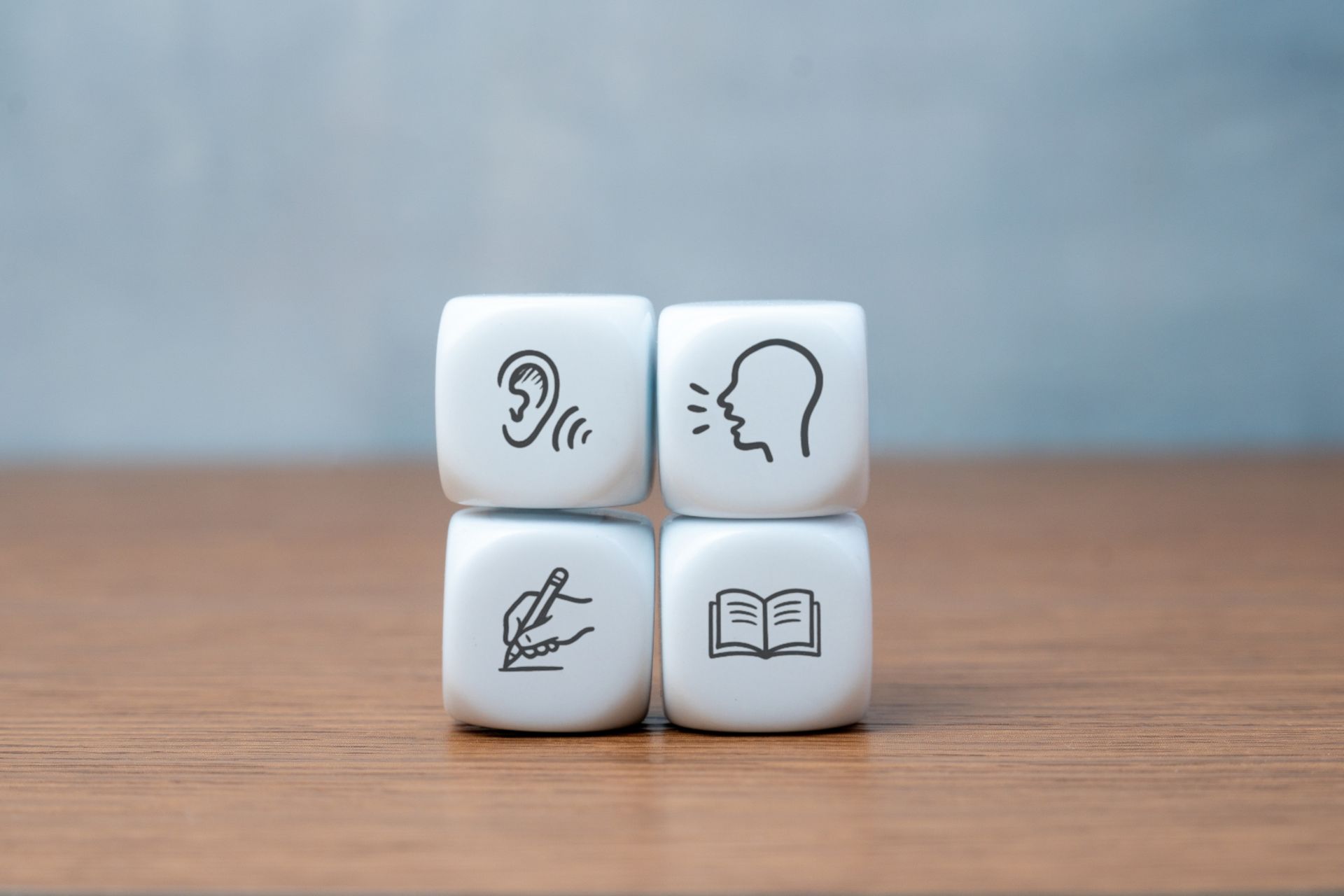 Four white cubes displaying icons for listening, speaking, reading, and writing skills. 