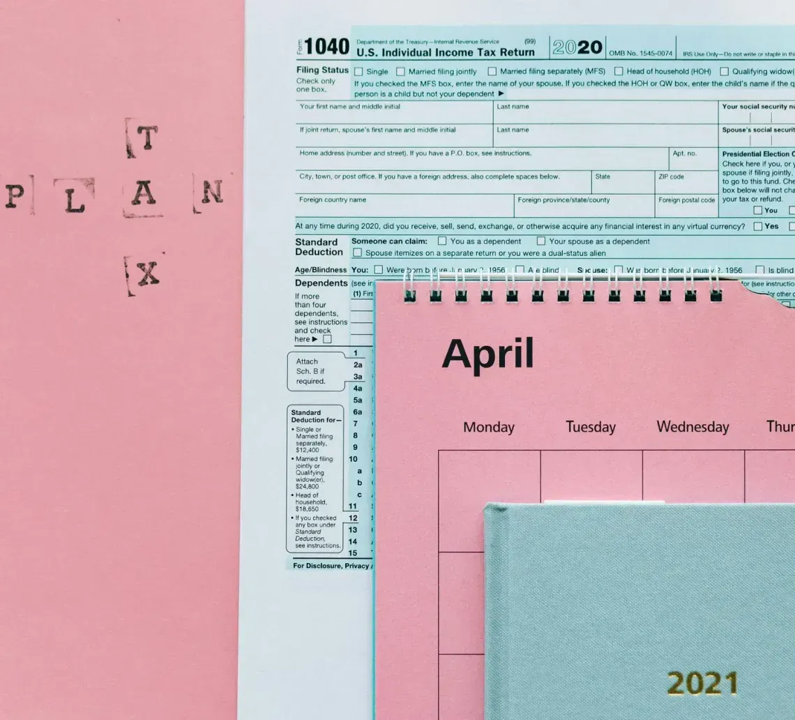 A US 1040 tax form, a pink calendar for April 2021, and a blue notebook, with the words 