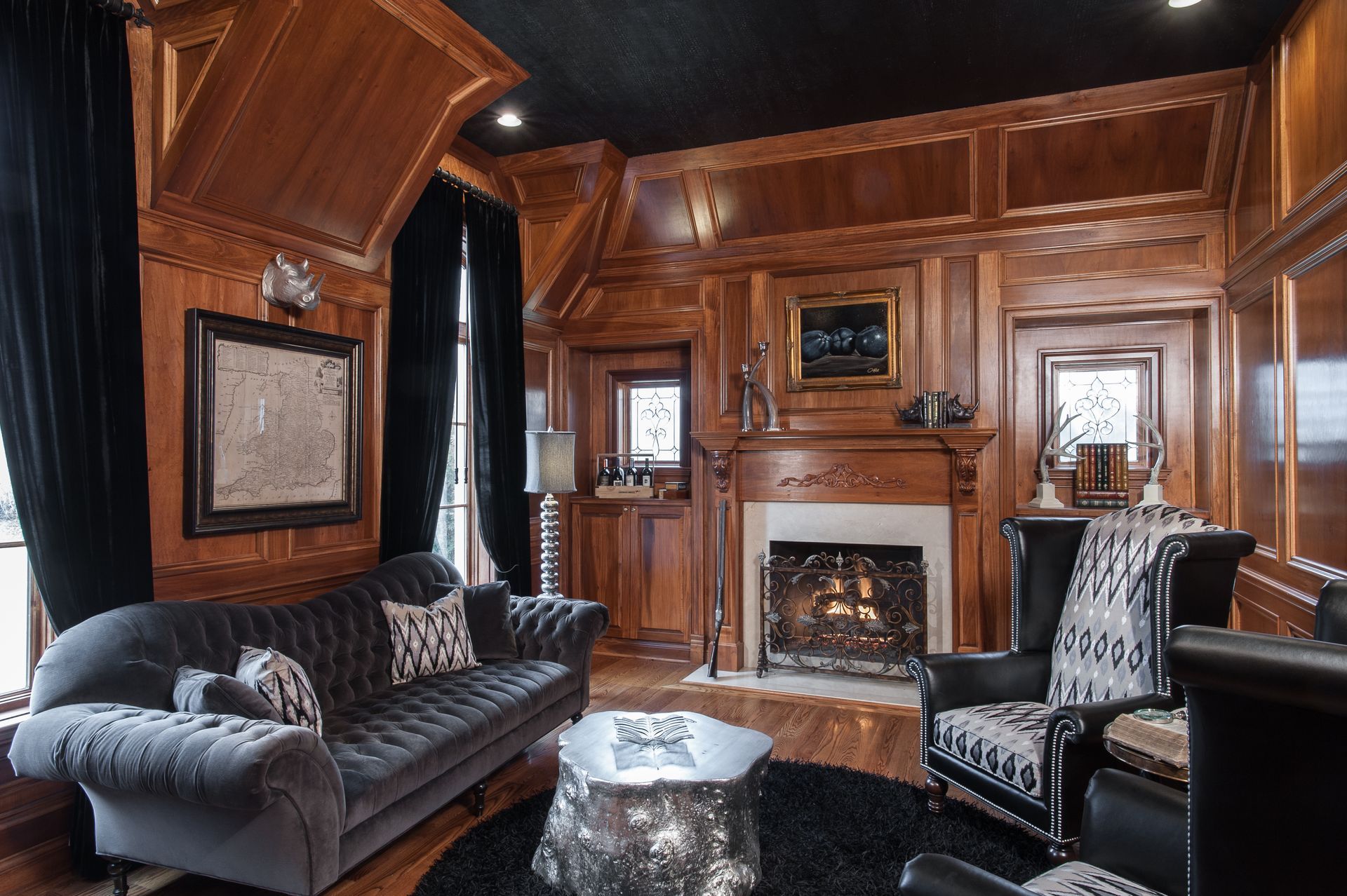 Elegant wood-paneled living room with fireplace, dark sofas, and large windows