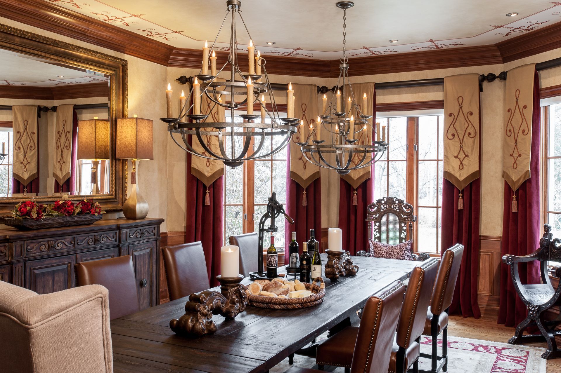 Elegant dining room with long table, chandeliers, red curtains, and fireplace mantel