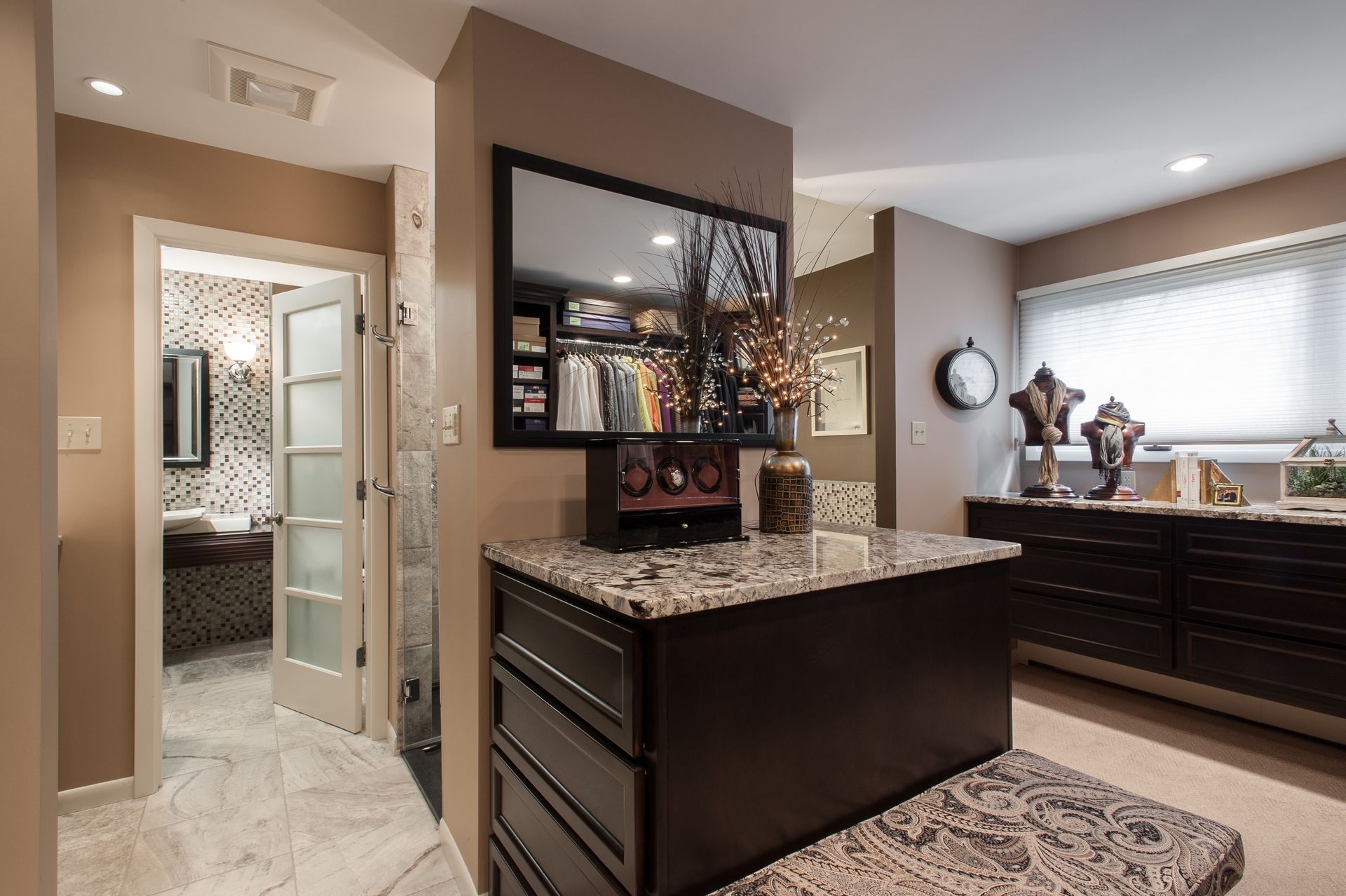 Modern kitchen with dark cabinets, granite island, and large mirror-like wall decor beside a bright bedroom doorway