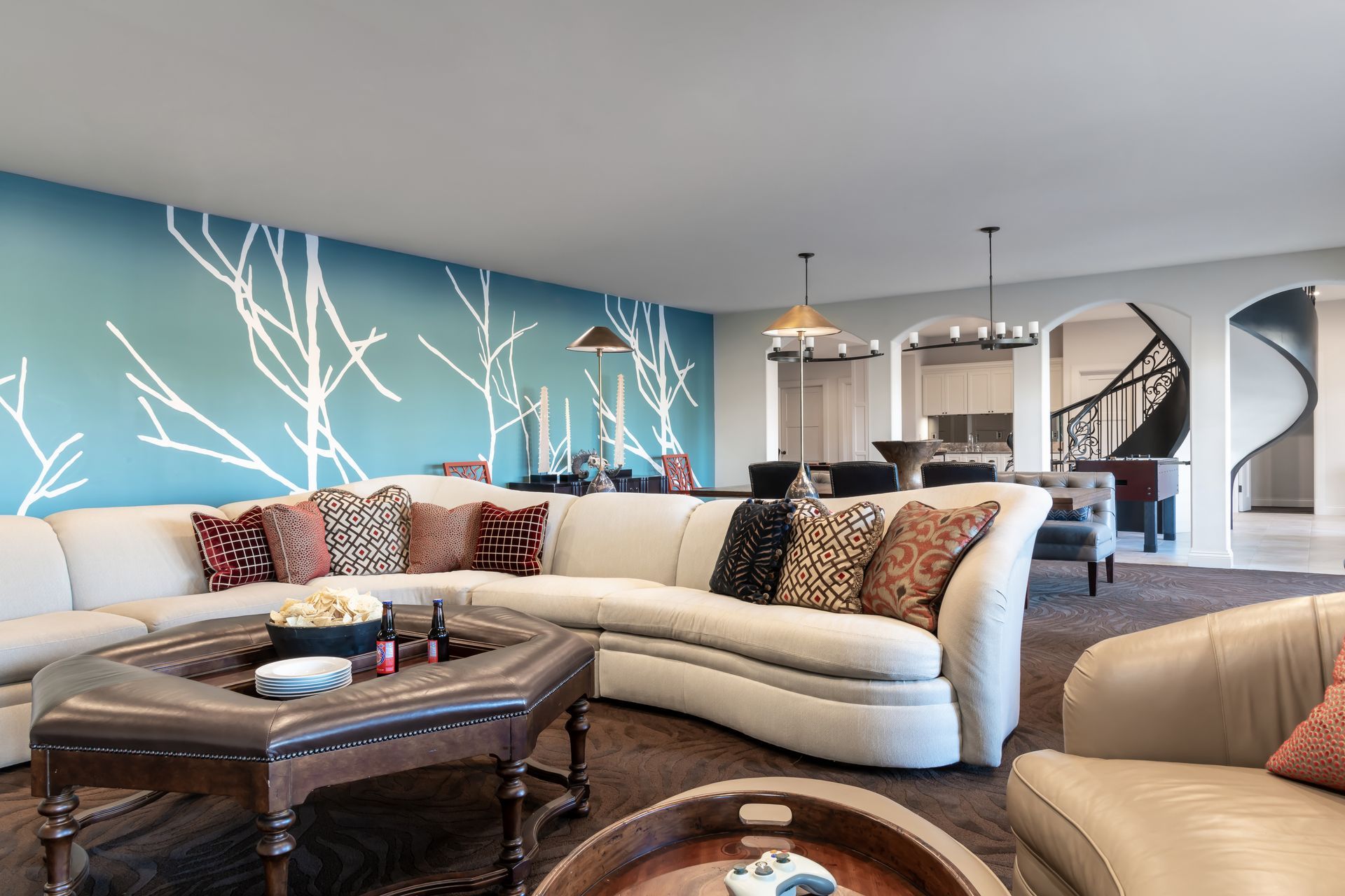 Modern living room with curved white sofa, coffee table, blue accent wall, and bar stools in the background