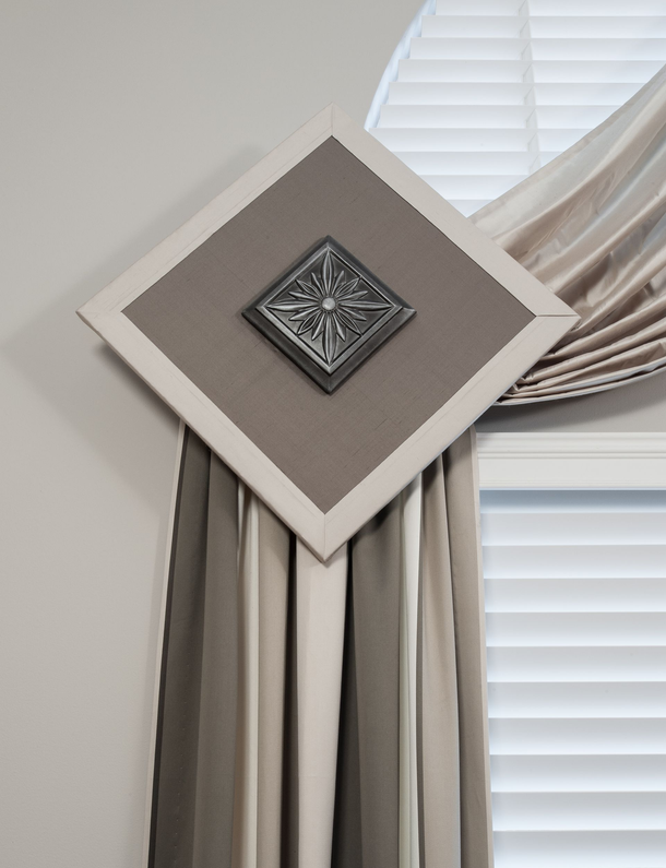 Decorative curtain tieback with square medallion holding cream and gray drapes by a window