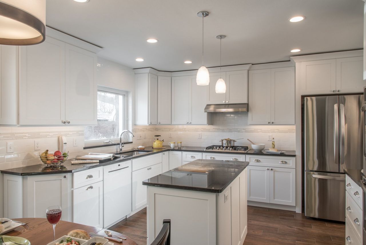 A kitchen with white cabinets , black counter tops , stainless steel appliances and a large island.