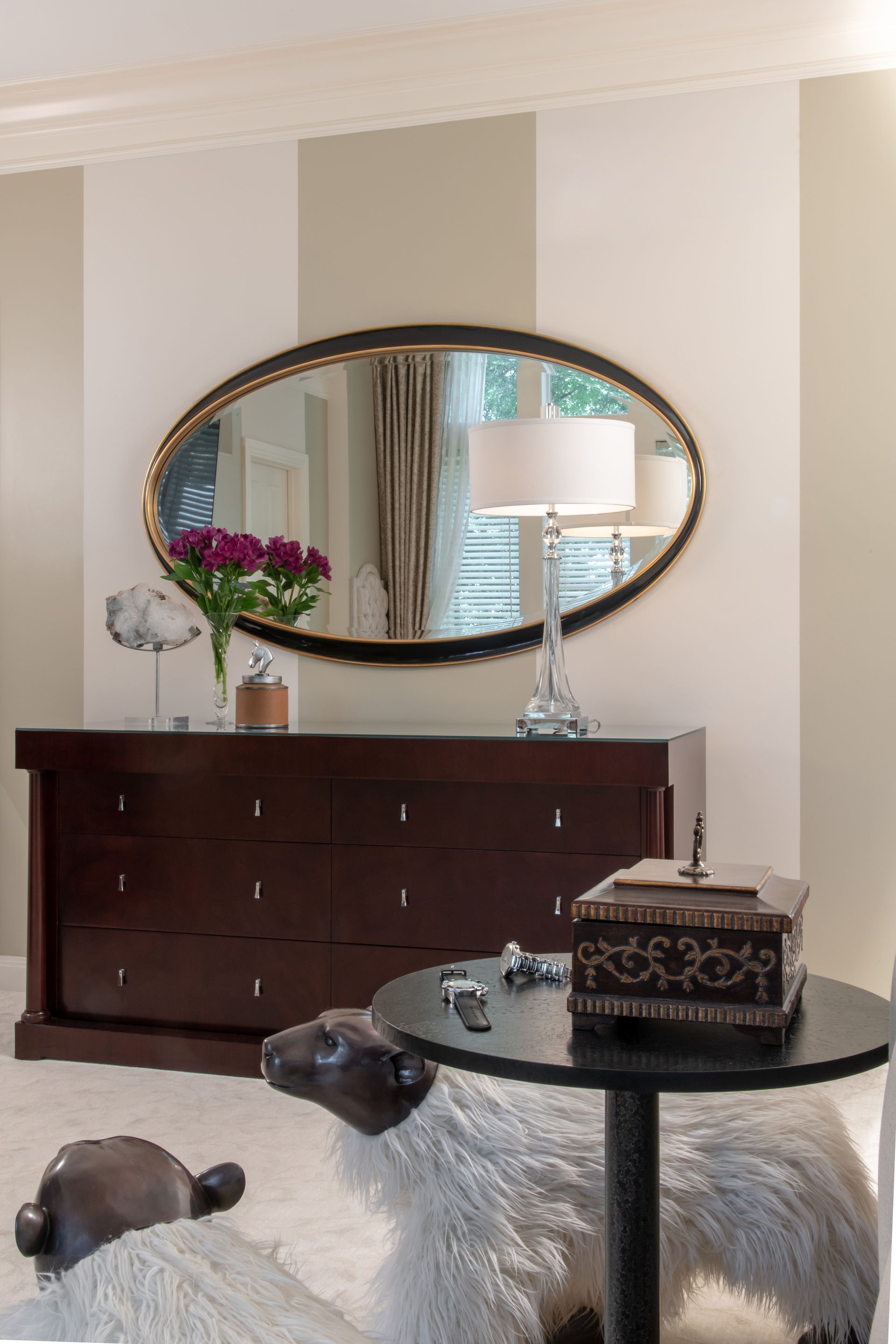 Elegant living room with oval mirror, dark dresser, flowers, and glass coffee table on a shaggy rug
