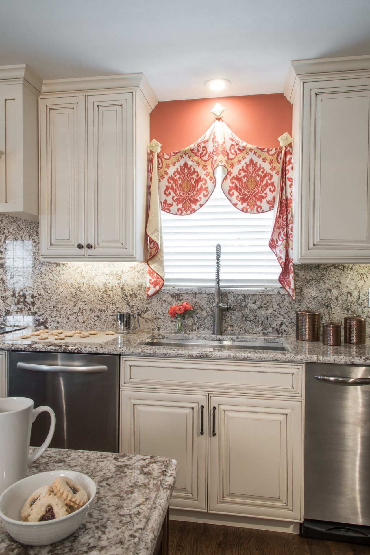 Kitchen with white cabinets, granite countertops, and a sink beneath a coral floral window valance.