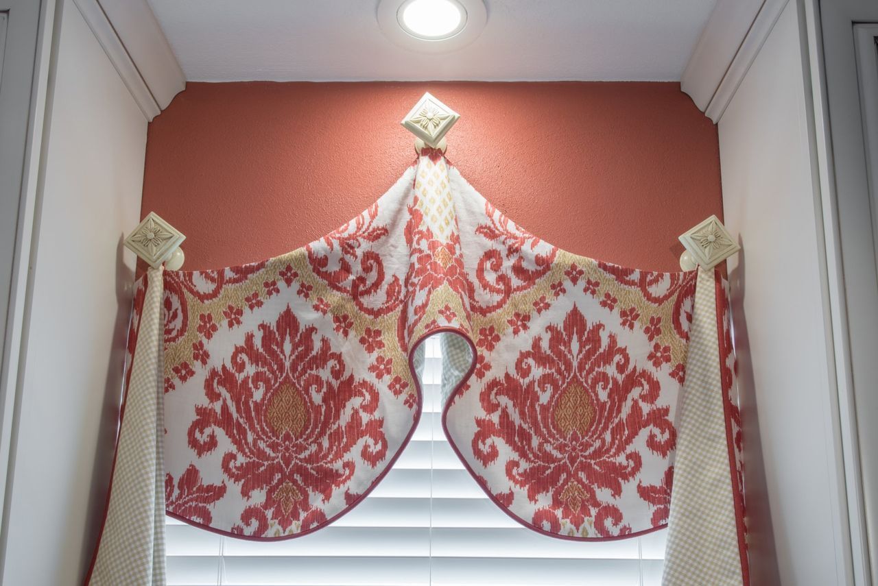White-and-red patterned valance curtains with draped swags over a window beneath a ceiling light.