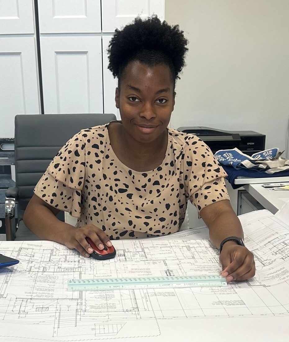 A woman is sitting at a desk looking at a blueprint.