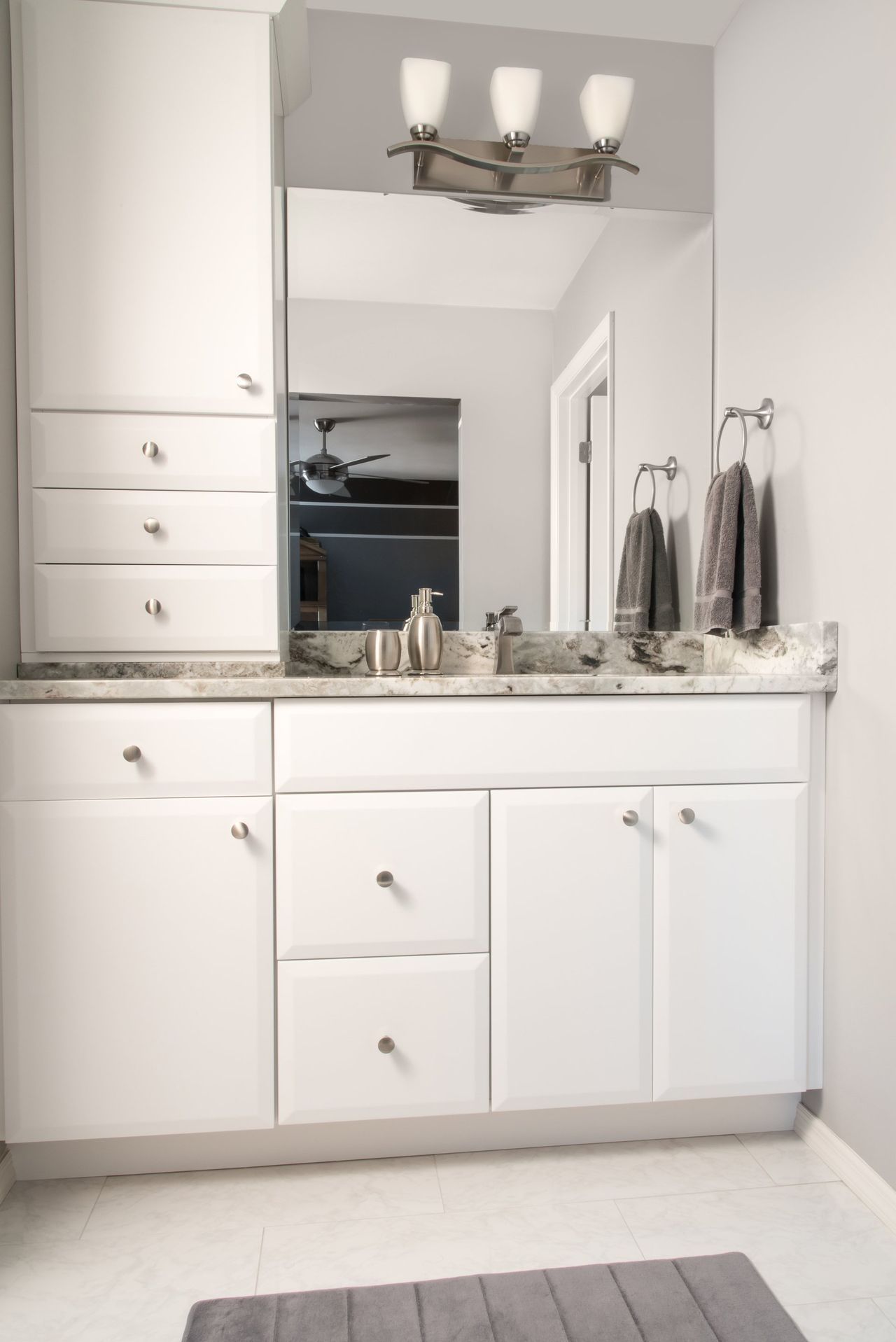 A bathroom with white cabinets and a large mirror.