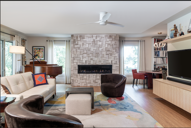 Modern living room with stone fireplace, sectional sofa, armchair, TV, and colorful area rug.