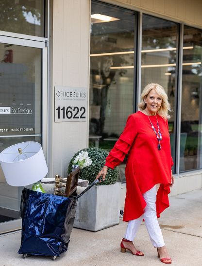 A woman in a red top is pushing a bag of furniture on a cart.