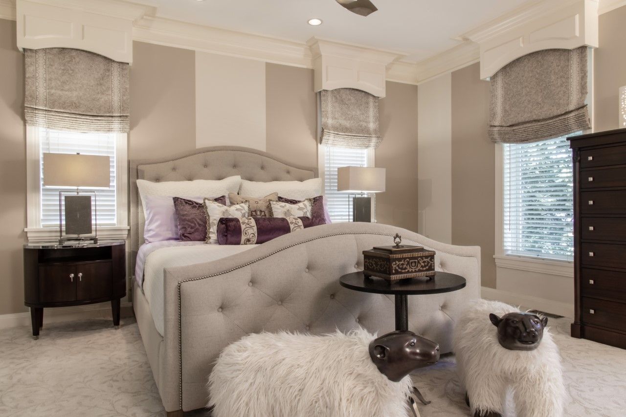 Elegant beige bedroom with tufted bed, mirrored nightstands, and fluffy bench in front of windows