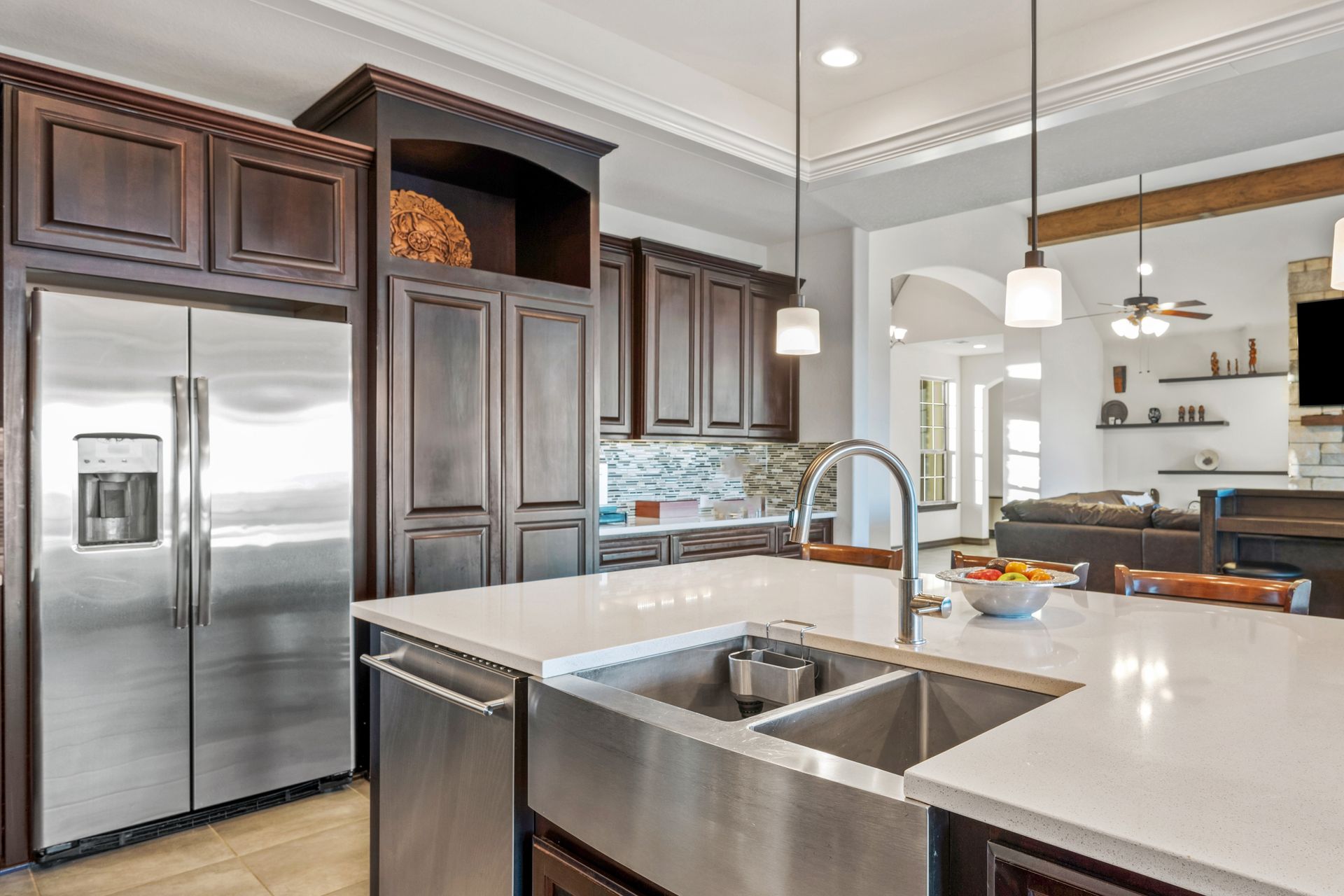 Modern kitchen with stainless steel appliances, dark wood cabinets, white island, and pendant lights
