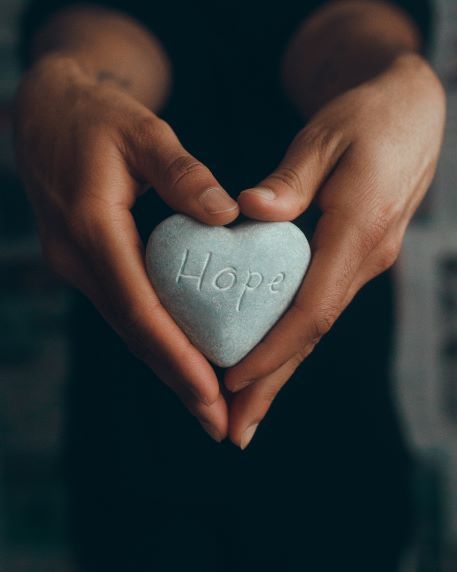Hands holding a gray heart-shaped stone engraved with “Hope”