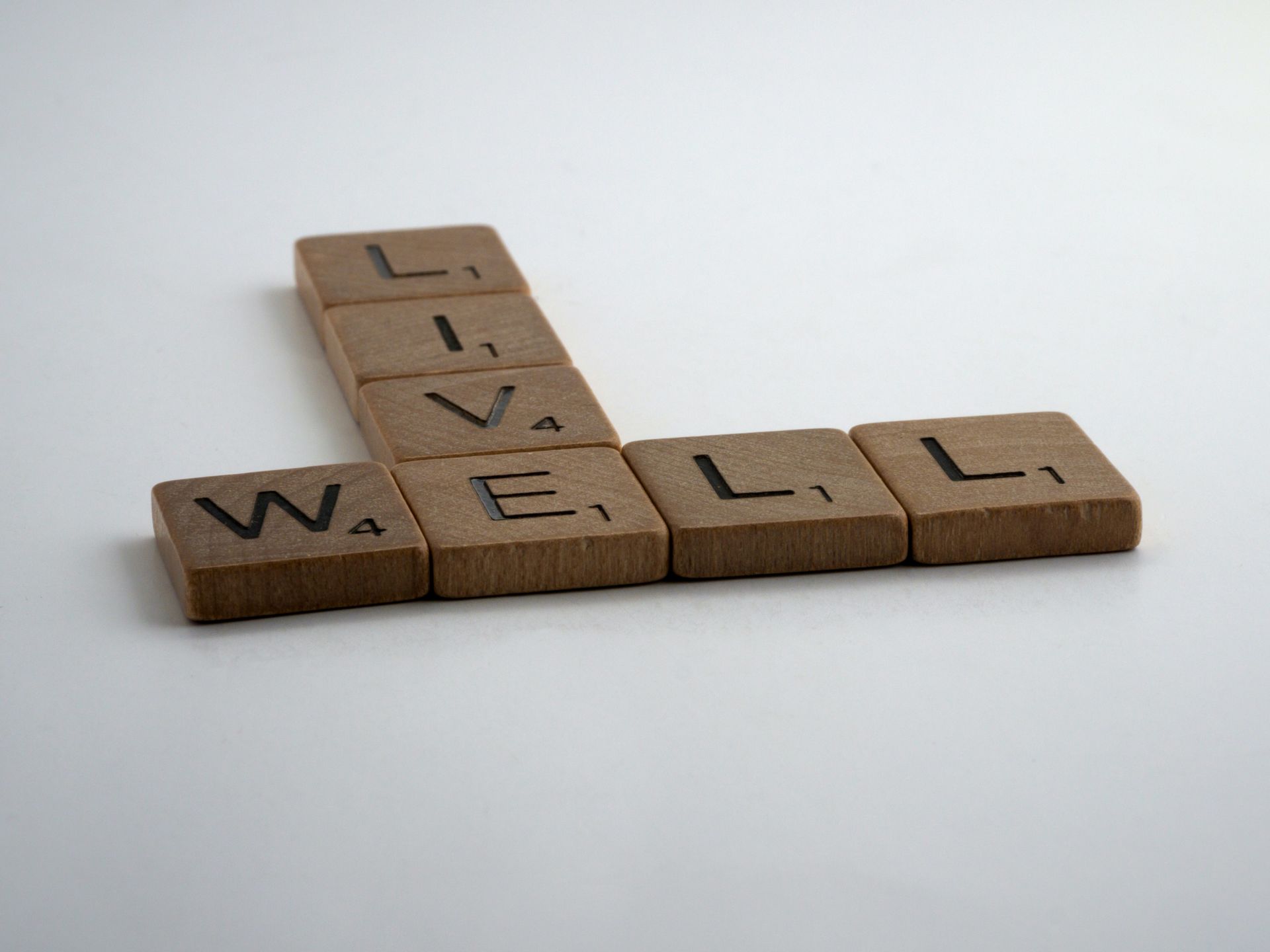 Wooden letter tiles spelling “WELL” and “LIVE” on a light background.