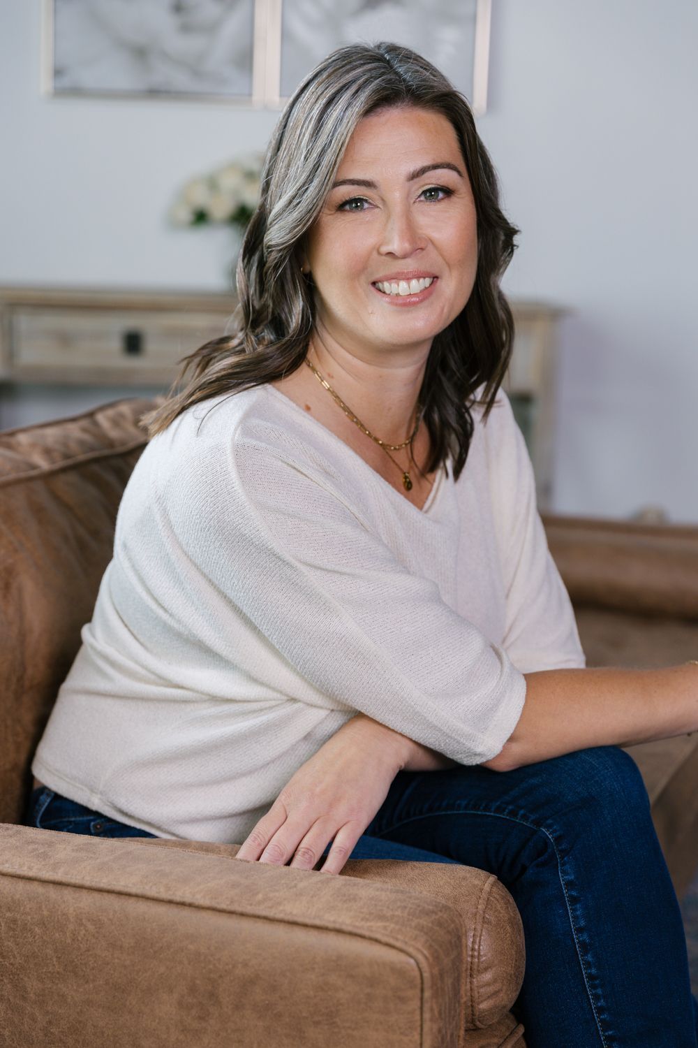 Smiling woman in a white sweater seated on a tan couch in a bright living room