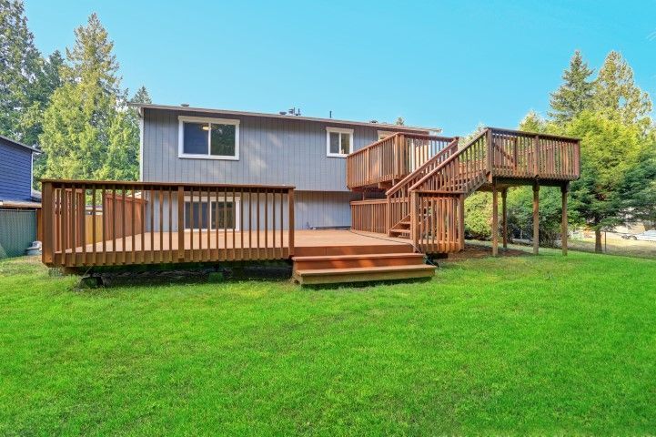 Backyard wooden deck with stairs and railing behind a house on a green lawn