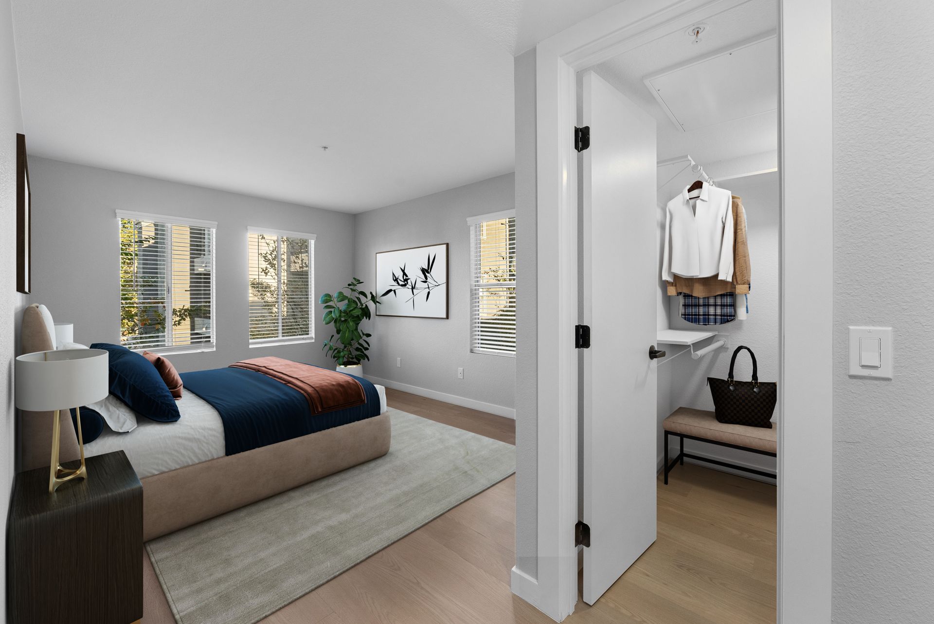 Bedroom with bed, closet, and windows; neutral colors, carpet, bench, and clothes.
