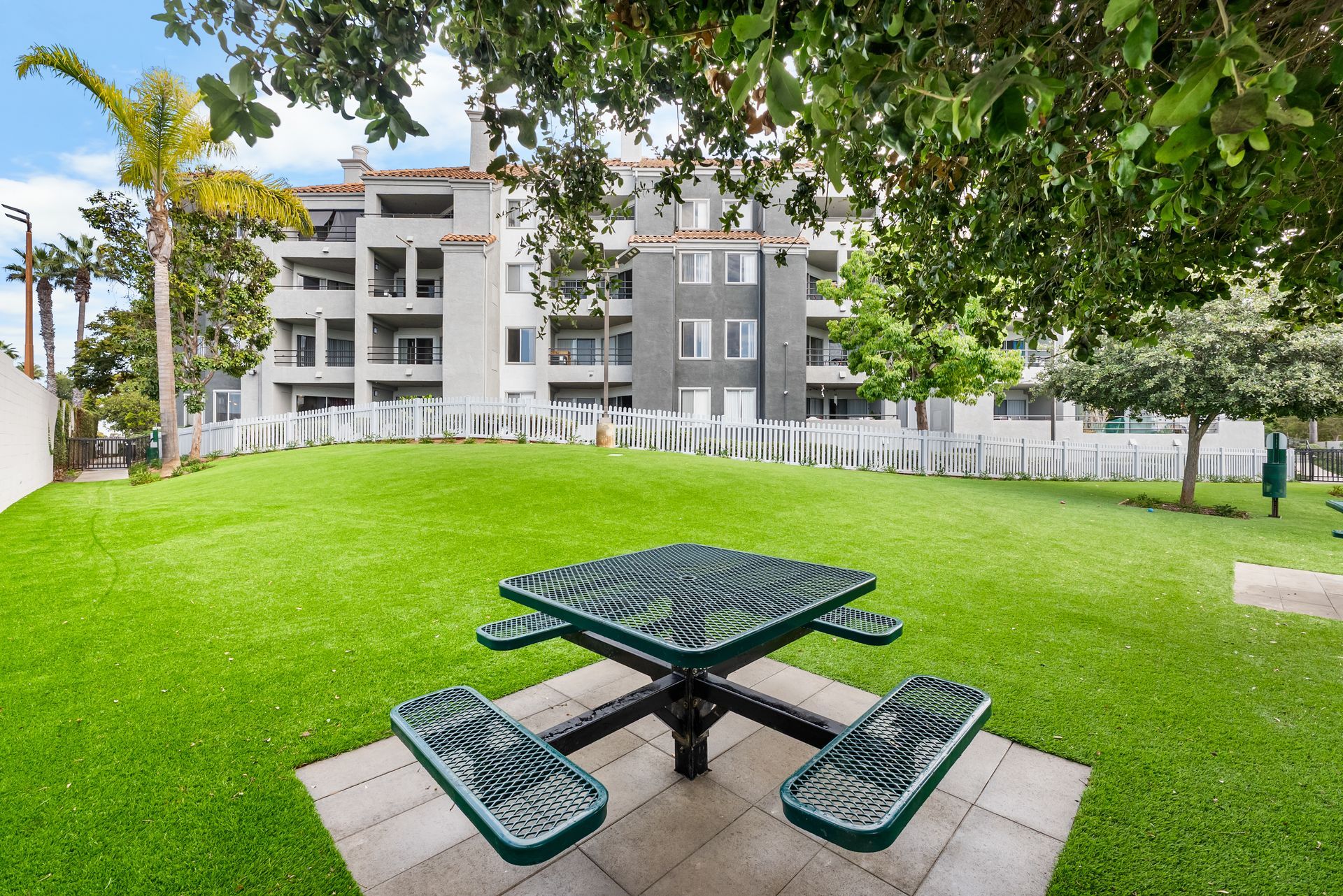 Picnic table on a grassy dog park lawn in front of a multi-story apartment building.