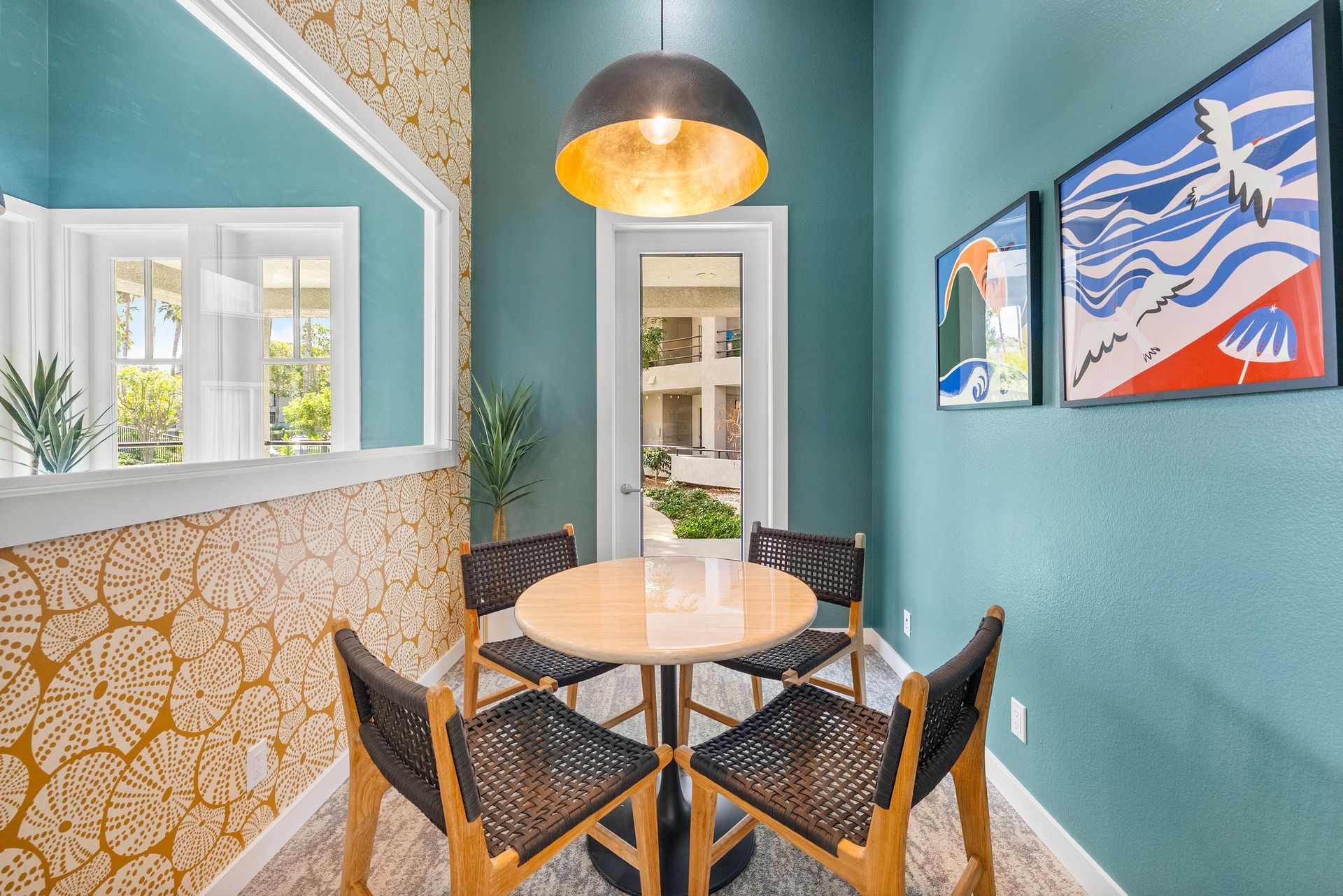 Small work area with a round table, four chairs, and art on blue walls, with a gold pendant light.