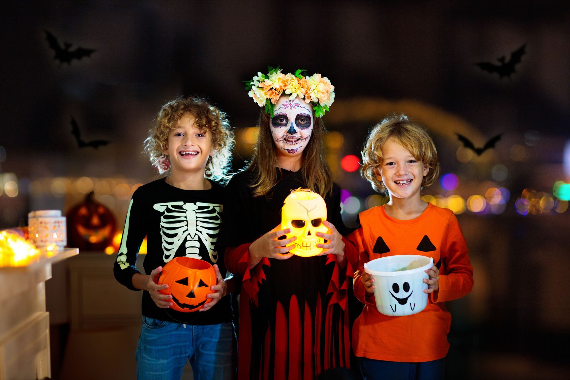 Three children in halloween costumes are holding pumpkins and a skull.