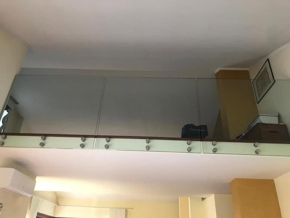 Interno di un loft con ringhiera in vetro, pareti bianche e un mobiletto color beige nell'angolo.