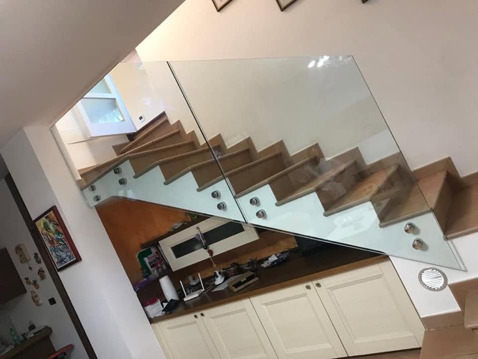 Scala moderna con ringhiera in vetro sopra una cucina bianca con mobili in legno.