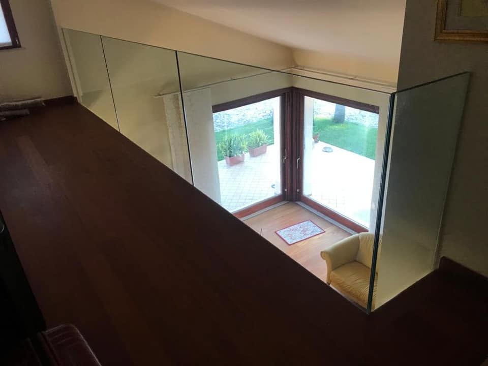 Balcone interno affacciato su un luminoso soggiorno con porte finestre e vista sul giardino.