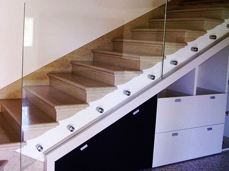 Scala moderna con ringhiera in vetro sopra armadi a muro.