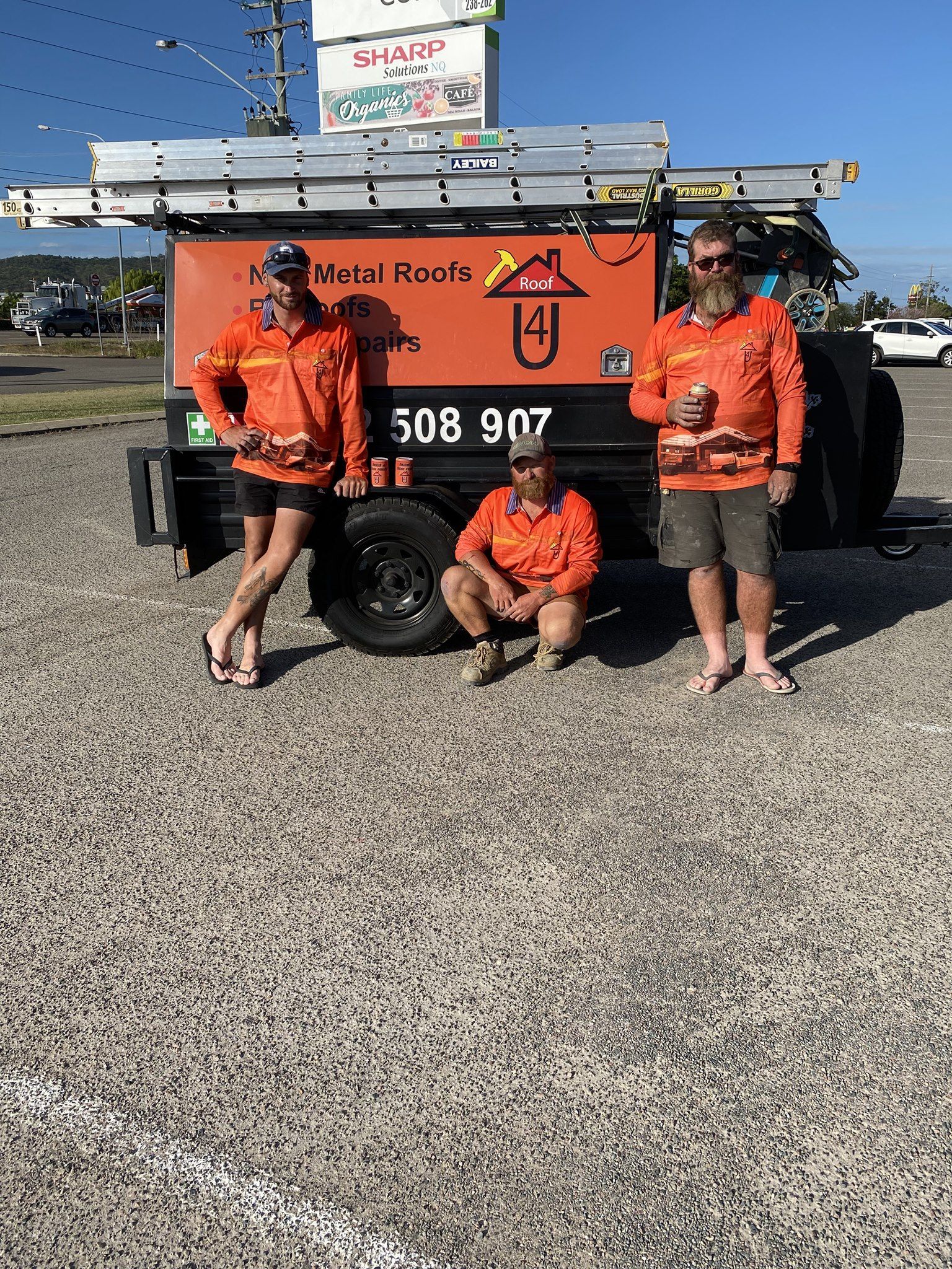 Three people in orange workwear pose in front of a trailer with 