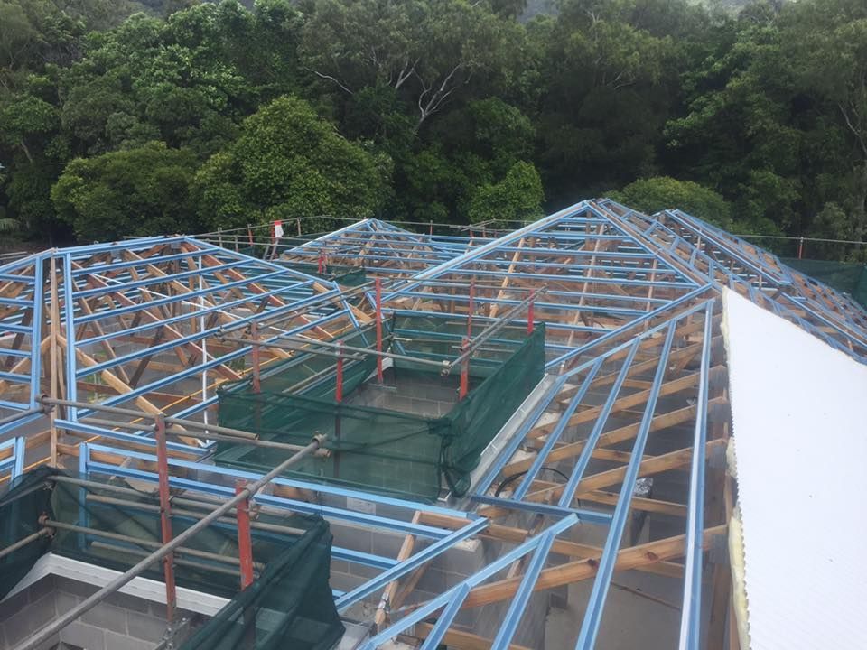 Roof construction: blue metal frame with wooden supports, green safety nets, and a wooded background.— Roof 4 U in Shaw, QLD