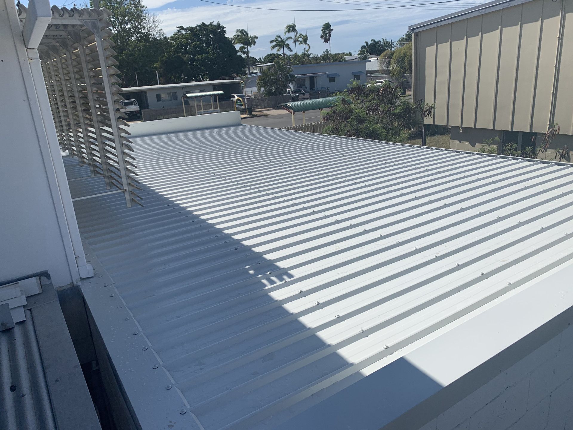 White corrugated metal roof on a building, with an adjacent structure and greenery in the background.— Roof 4 U in Alice River, QLD