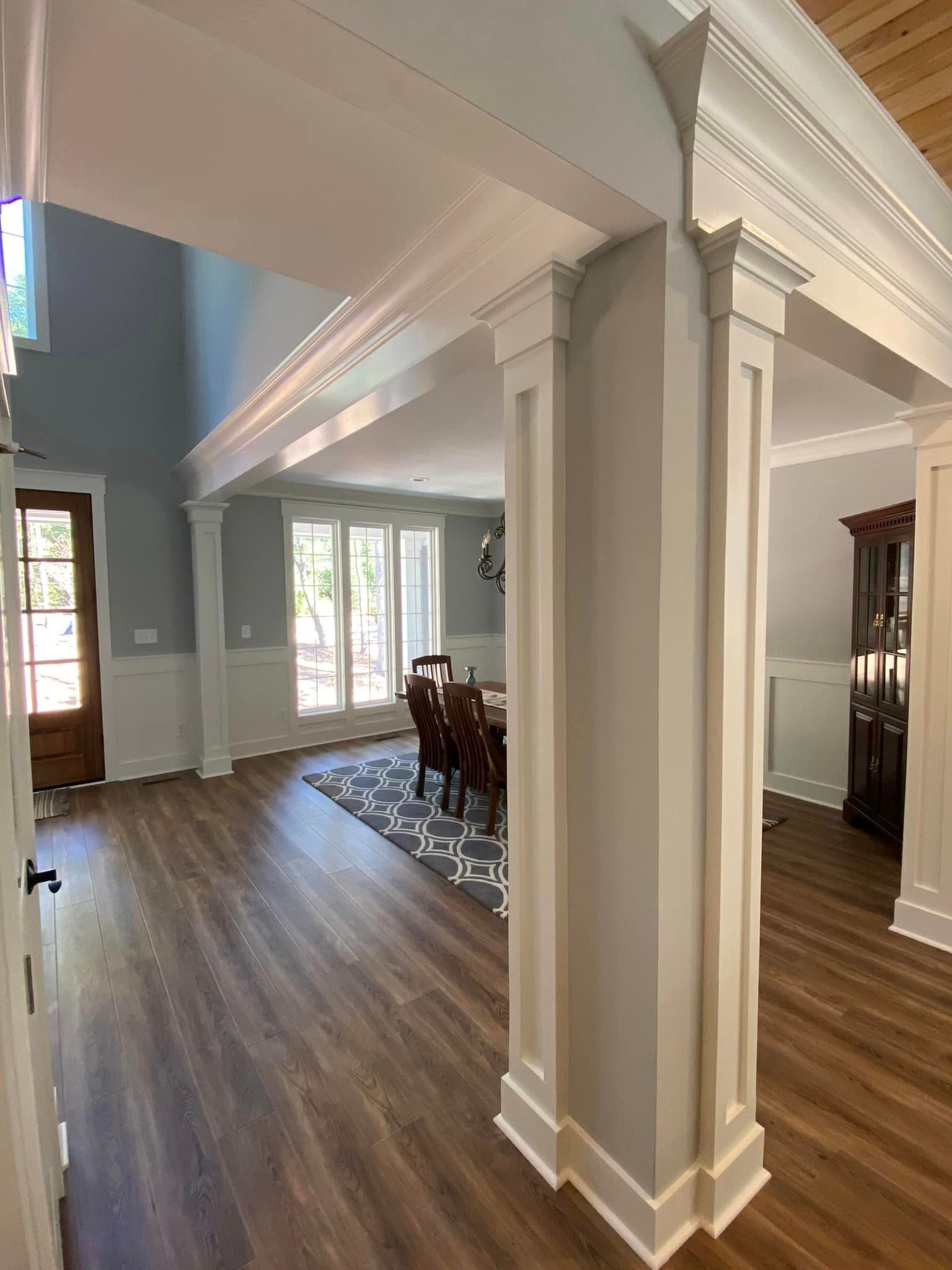a living room with hardwood floors , columns , a table and chairs .