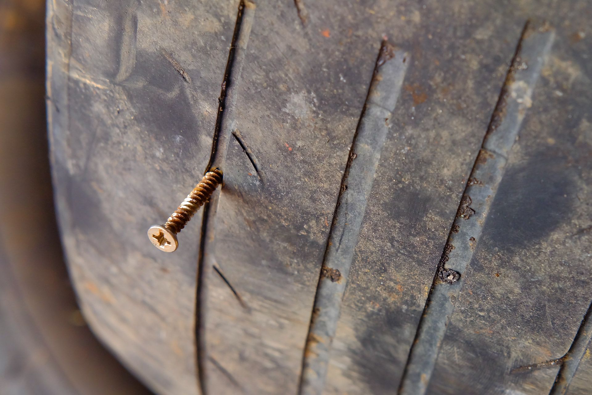 Close-up of a worn tire tread with a rusty screw embedded in it
