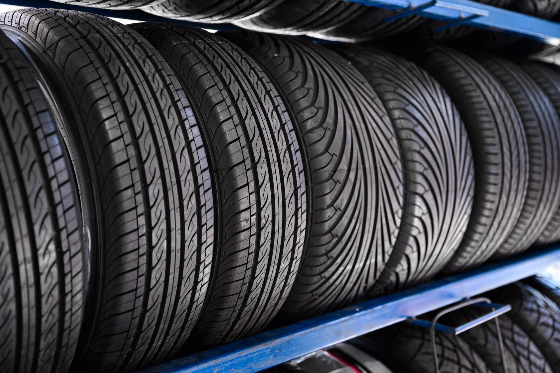 Stacked black tires on blue metal shelves in a warehouse.